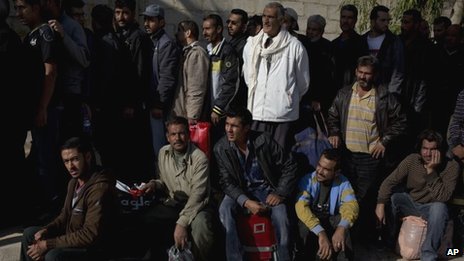 Men wait to be searched by the Syrian military